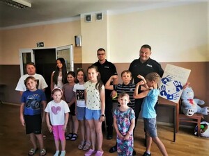 dwóch policjantów w umundurowaniu służbowych stoi z grupą dzieci w różnym wieku