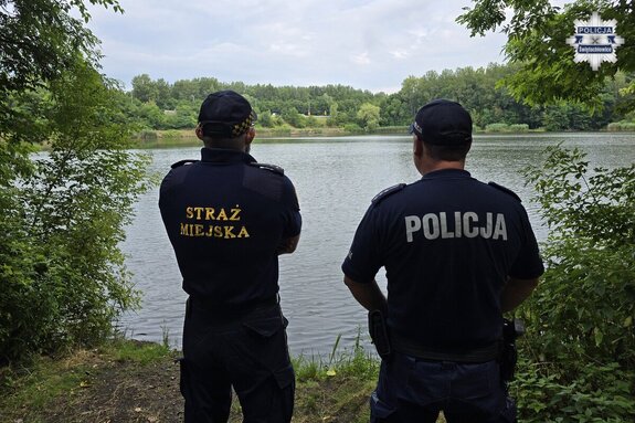 policjant i strażnik miejski w umundurowaniu służbowym stoją przy brzegu zbiornika wodnego