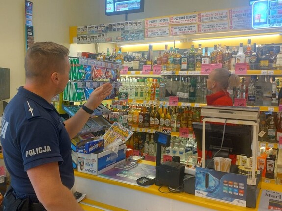 policjant w mundurze stoi przed ekspedientką sklepu ze stoiskiem z alkoholem