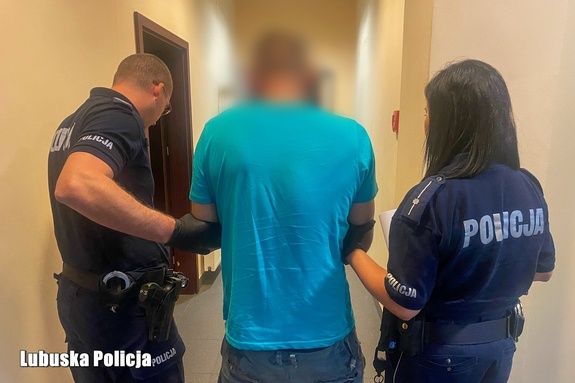 Widziani od tyłu w korytarzu komisariatu dwójka policjantów prowadzących zatrzymanego mężczyznę