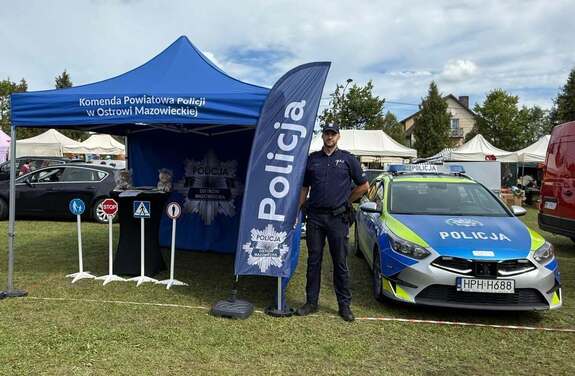 Stoisko wystawiennicze pod namiotem obok policjant i radiowóz