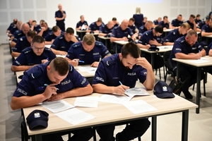 grupa policjantów siedzi przy stolikach i rozwiązują testy wiedzy