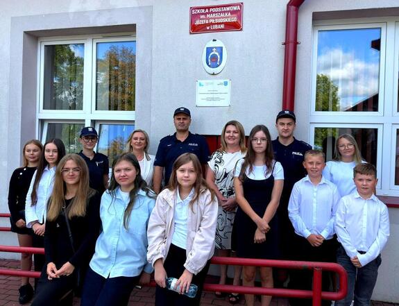 Pozująca na tle budynku szkoły grupa młodzieży oraz dwóch policjantów