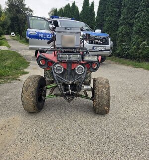 Na wąskiej drodze na tle zieleni quad a za nim radiowóz terenowy