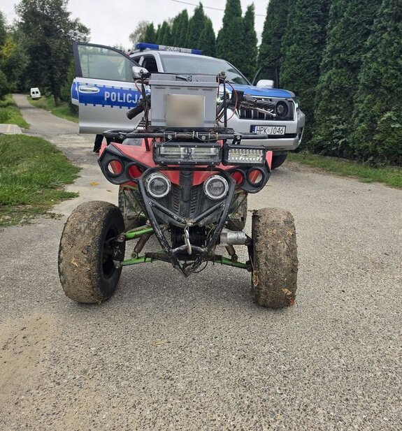 Na wąskiej drodze na tle zieleni quad a za nim radiowóz terenowy