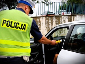 Zbliżenie policjanta podającego do użytku alkotest przez uchylone drzwi samochodu osobowego