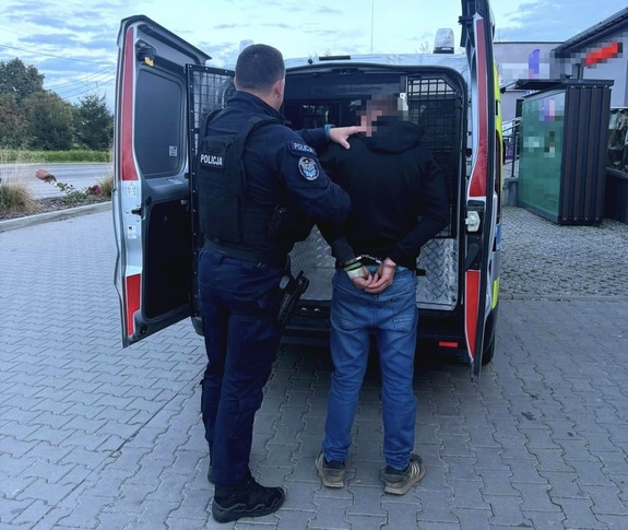 Policjant wprowadzający zatrzymanego do przedziału transportowego radiowozu typu bus