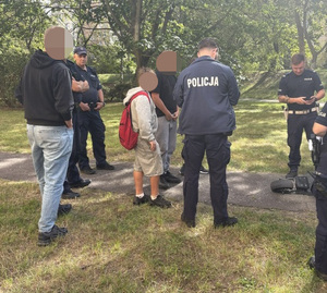 W parku widziani z tyłu policjanci, młody człowiek i ludzie po cywilnemu
