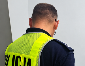 Odwrócony plecami policjant w kamizelce odblaskowej w pomieszczeniu