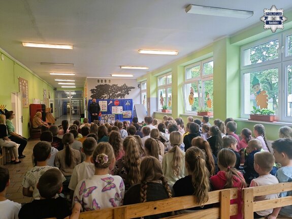 Policjant podczas pogadanki dla dzieci w auli szkolnej