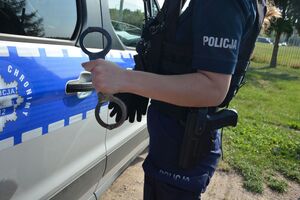 Zbliżenie ręki policjanta z kajdankami na tle radiowozu