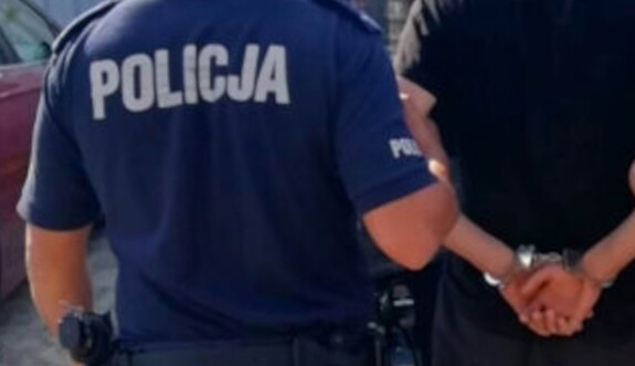 Zdjęcie pleców policjanta i mężczyzny ze skutymi rękami