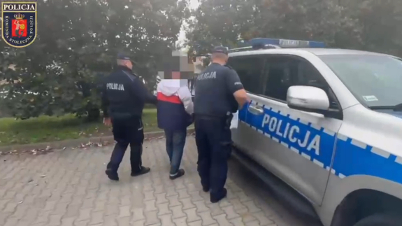 Widziani od tyłu dwaj policjanci doprowadzający do radiowozu mężczyznę ze skutymi rękami