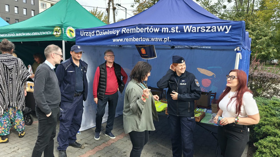 Obok namiotu wystawienniczego ludzie w różnym wieku oraz dwójka policjantów