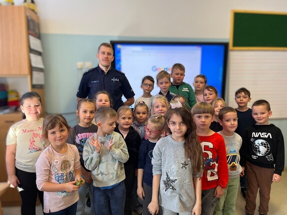 Policjant pozujący do zdjęcia z grupą dzieci w sali szkolnej