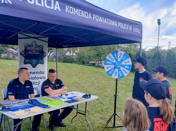 Dwaj policjanci w namiocie wystawienniczym, obok grupa młodzieży