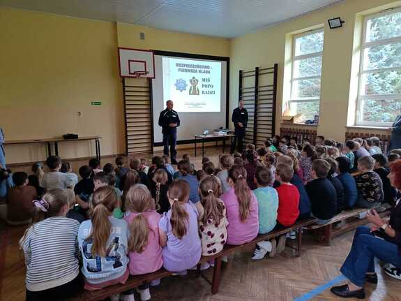 Dwóch policjantów podczas prelekcji w sali gimnastycznej z licznie zgromadzonymi dziećmi i młodzieżą