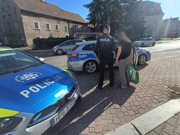 Dwa radiowozy na ulicy obok policjant i mężczyzna ze zanimizowaną twarzą