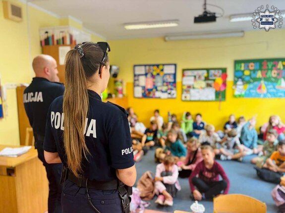 Dwójka policjantów prowadząca pogadankę dla dzieci zgromadzonych w sali lekcyjnej