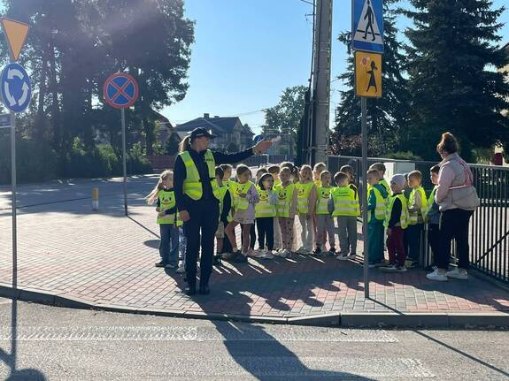 Policjantka z wychowawczynią oraz grupą przedszkolaków przed przejściem dla pieszych