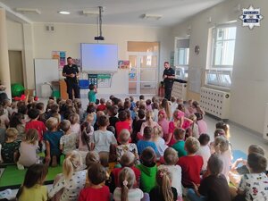 Dwaj policjanci podczas pogadanki dla dużej grupy dzieci zgormadzonej w sali przedszkolnej