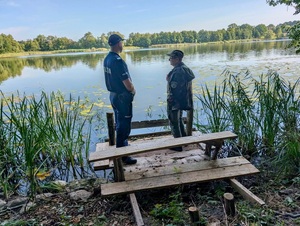 Na drewnianym pomoście nad wodą policjant i strażnik rybacki