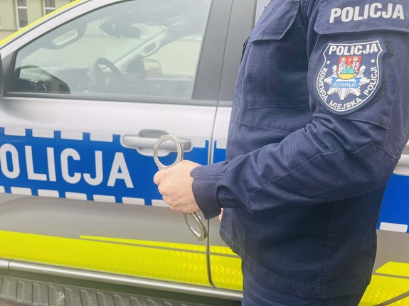 Sylwetka policjanta trzymającego w ręce kajdanki na tle radiowozu
