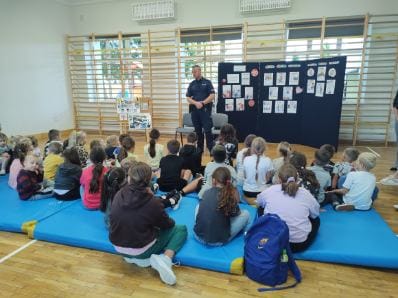 Policjant prowadzący pogadankę dla siedzących w sali gimnastycznej dzieci