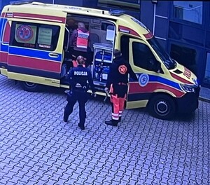 Policjant wraz z ratownikami medycznymi stojący przed karetka pogotowia ratunkowego.