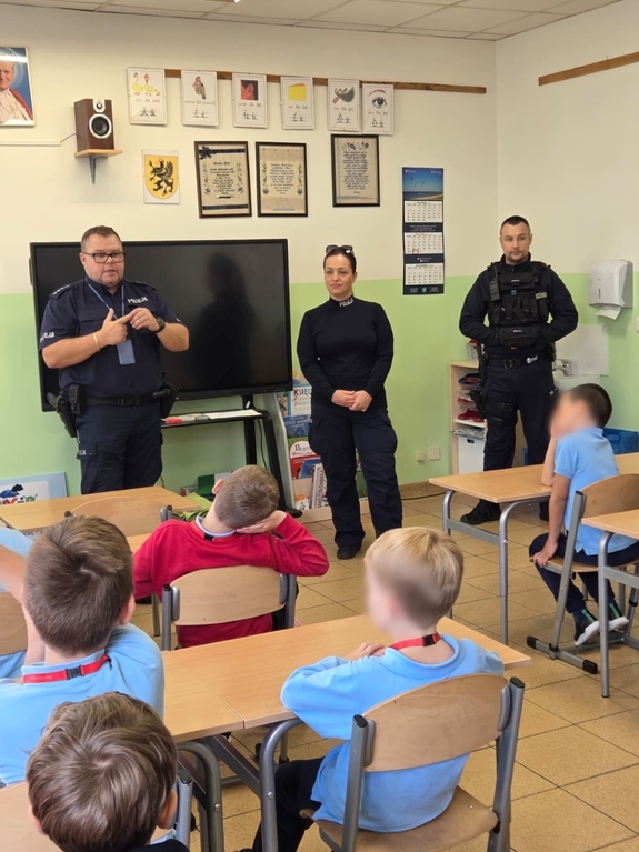 Zdjęcie przedstawiające troje policjantów w klasie szkolnej podczas zajęć lekcyjnych prowadząc prelekcję.
