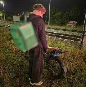 W scenerii nocnej na tle torów kolejowych i zieleni młody mężczyzna z rowerem