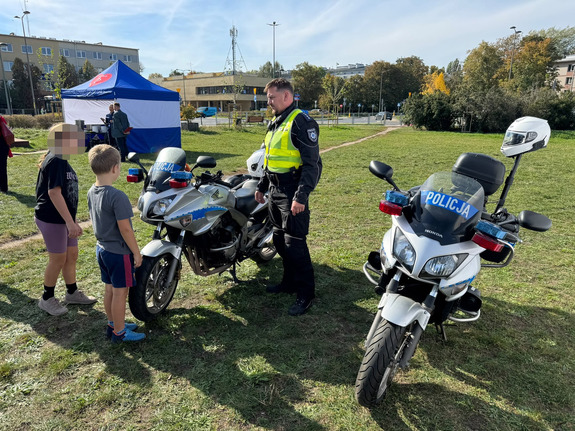 Piknik na terenach zielonych, na pierwszym planie dwa motocykle policyjne i policjant oraz małe dzieci