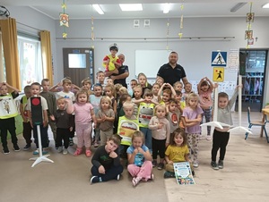 Grupa przedszkolaków pozująca wewnątrz sali do zdjęcia wraz z dwoma policjantami