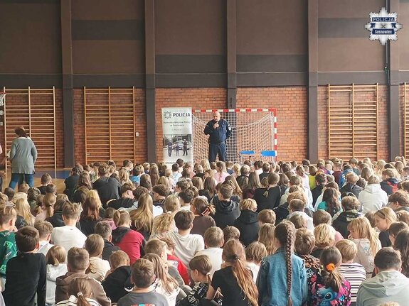 Policjant podczas prelekcji do licznie zgromadzonej młodzieży w sali gimnastycznej