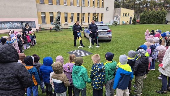 Grupa dzieci z przedszkola, w tle widać dwóch policjantów i radiowóz policyjny.