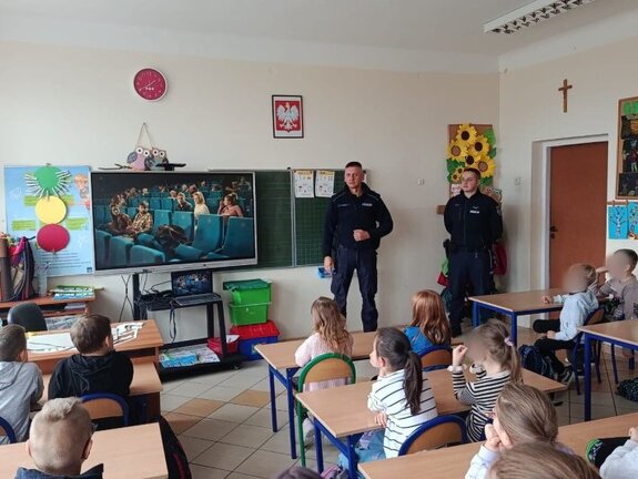 Zdjęcie przedstawiające policjantów w klasie szkolnej prowadzących rozmowę z dziećmi.